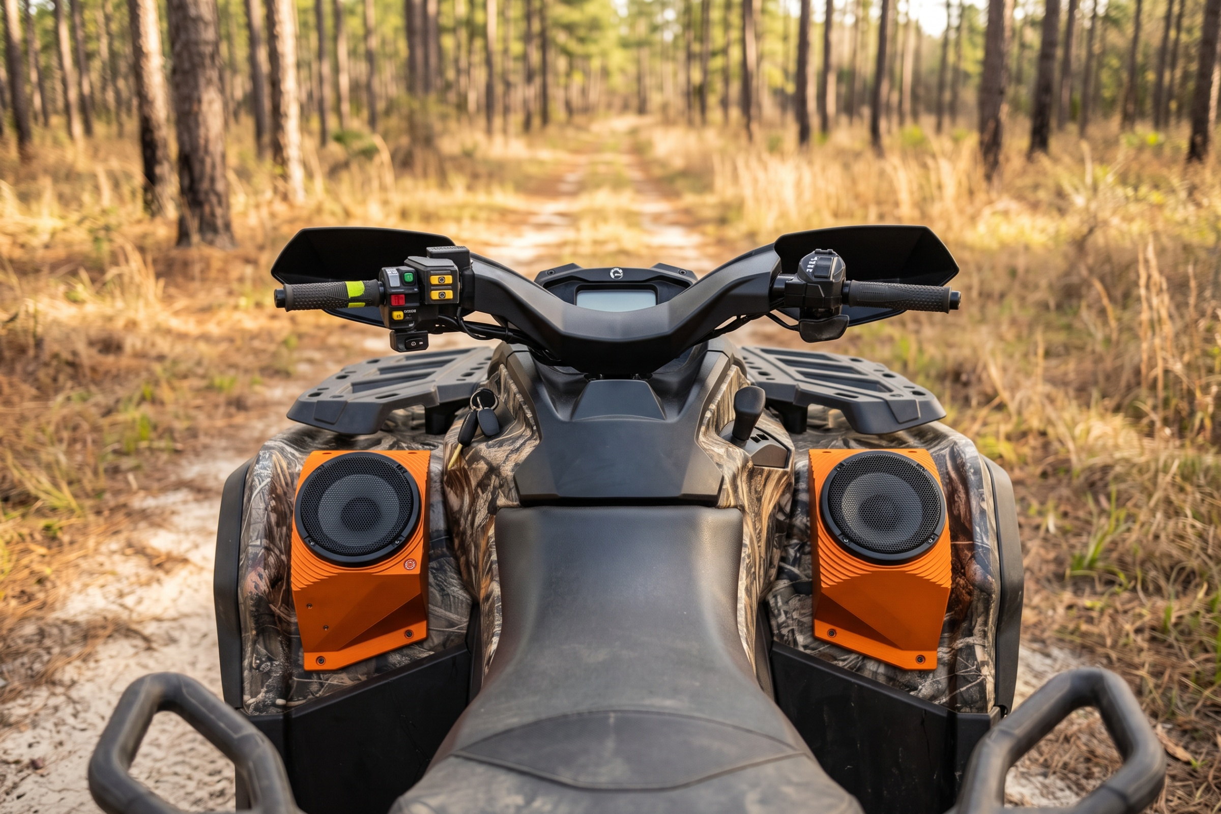 Twin custom orange fender-pod speaker enclosures on a camo ATV on a pine trail — installed by Sturgess Customs